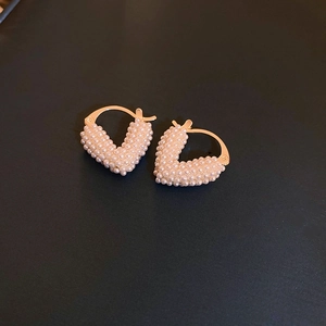 Detailed view of V-shaped gold earrings with white pearl inlay on black background