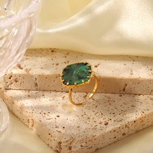 Detailed view of a gold square ring with green turquoise stone set on beige silk fabric