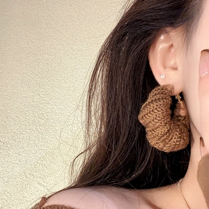 Close-up of a model wearing brown knitted hoop earrings with a warm autumn aesthetic