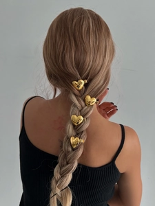 Détail de quatre pinces à cheveux dorées en forme de cœur sur une queue de cheval tressée