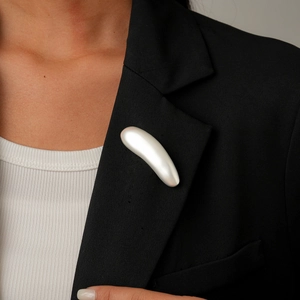 Close-up of a minimalist silver teardrop brooch on a professional black blazer