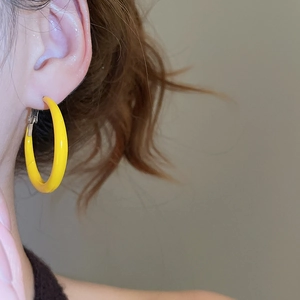 Gros plan d'une grande boucle d'oreille ronde jaune portée sur l'oreille