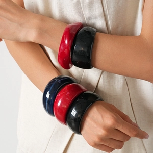 Close-up of model wearing stacked chunky acrylic bangles in red, black, and navy blue