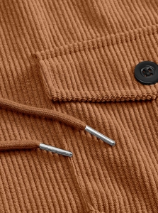 Macro shot of brown corduroy jacket detail with buttoned flap pocket and metal-tipped drawstrings