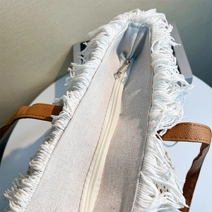 Detail shot of the woven bag edge with white tassels, brown handle, and silver zipper