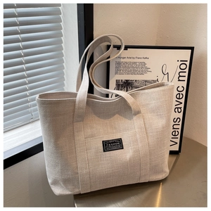 Detail of oat-colored canvas tote bag featuring fashion lettering in natural light