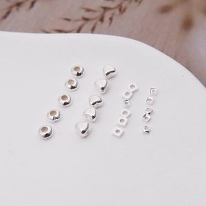 Detailed view of silver S925 spacer beads in various geometric shapes on a white plate