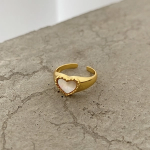 Detailed close-up of a golden heart ring with a white shell inlay on a stone surface