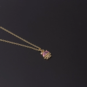 Detail of a golden jellyfish pendant necklace with pink crystal and zircon on black background