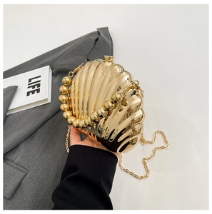 Detail of a golden shell evening bag with pearl bead handle and metallic stripe finish