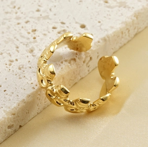 Détail d'une bague ouverte dorée avec motifs floraux gaufrés sur support en travertin