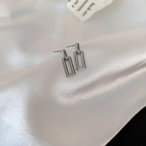 Macro shot of silver geometric interlocking rectangular earrings on white silk fabric