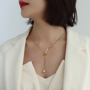 Elegant gold pin necklace with pearl fringe pendant worn by a model in a white blazer