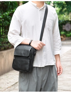 Close-up of a minimalist black genuine leather men's crossbody bag on a model outdoors