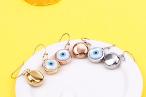 Evil eye earrings in gold, silver, and rose gold hanging on a white ceramic plate