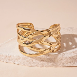 Detailed view of layered crossover gold cuff bracelet on a white textured stone pedestal