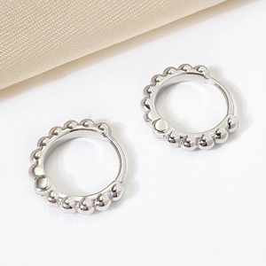 Minimalist silver beaded hoop earrings with metallic finish on elegant fabric background