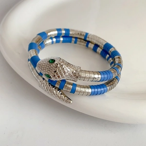 Close-up of a silver and blue coiled snake bracelet with green gemstone eyes on ceramic
