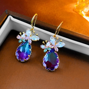 Detail view of gold earrings with butterfly zircon and waterdrop-shaped blue gradient gemstone