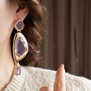 Close-up of vintage gold earrings with irregular purple resin stones on a model