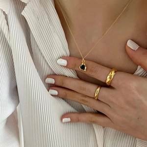 Close-up of a gold heart pendant necklace and quilted ring worn on a pleated shirt