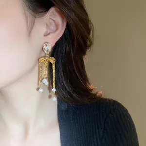 Boucles d'oreilles élégantes goutte d'eau avec strass, pompon doré et perles sur modèle