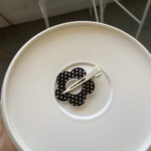 Close-up of a black acrylic flower hair clip with white polka dots on a white surface