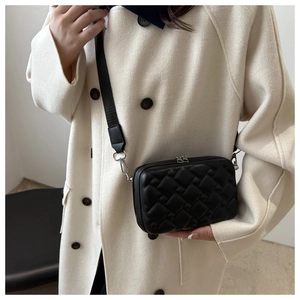 Detail of black quilted crossbody bag with silver hardware on beige coat
