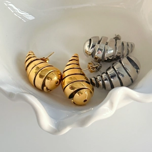 Abstract spiral hollow hoop earrings in gold and silver finish on a white ceramic plate