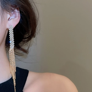 Detailed close-up of long gold fringe tassel earrings with shimmering crystals on model
