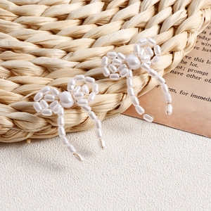 Close-up of handmade faux pearl bow earring featuring detailed woven craftsmanship and luster