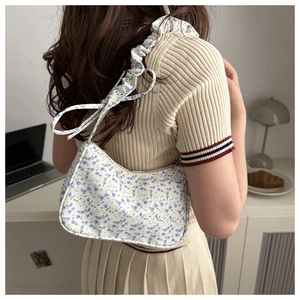 Floral print underarm bag with ruffled shoulder strap shown on a model's shoulder