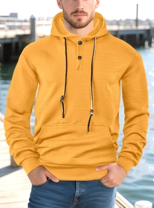 Detail of men's yellow waffle knit hoodie showing black button placket and texture