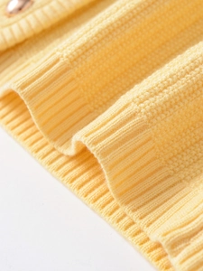 Macro shot of pale yellow knit cardigan showing waffle texture and metallic button detail