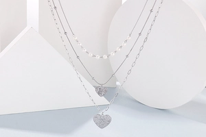 Detailed view of silver layered necklace with pearls and textured heart pendants on a display