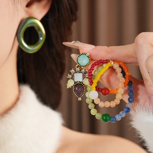 Close-up of vintage glass flower earrings and colorful beaded rings held by a model