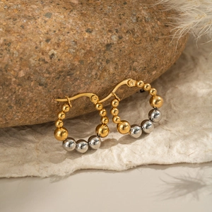 Two-tone beaded gold and silver hoop earrings on brown stone with feather accent