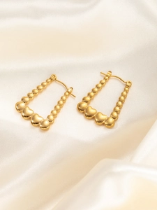 Detailaufnahme der goldenen Herz-Ohrringe mit Perlen auf weichem Satin-Hintergrund