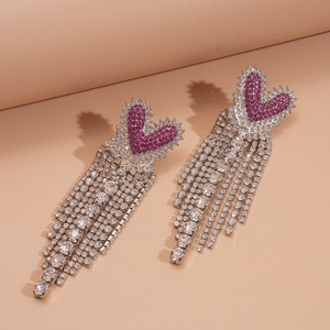 Détail de boucles d'oreilles cœur avec longs glands et strass roses et argentés brillants