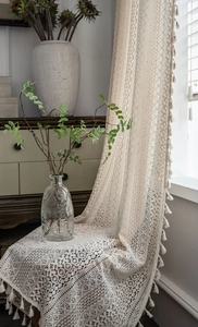 Close-up of beige crochet lace curtain featuring hollow floral patterns and fringe tassels