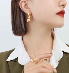 Gros plan de boucles d'oreilles dorées au design lave portées par un mannequin en tenue chic