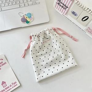 Close-up of white polka dot drawstring pouch with pink ribbons on a clean desktop