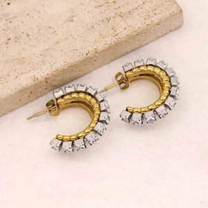 Close-up of gold C-shaped earrings with inlaid rows of clear diamonds on stone background