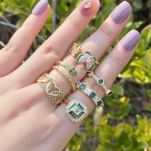 Close-up of gold rings set with emerald zircon and butterfly designs on a hand