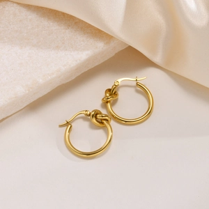 Detail of golden knotted hoop earrings on elegant white marble and silk texture