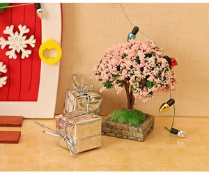 Détail d'un sapin de Noël miniature avec fleurs roses et cadeaux argentés dans une maison
