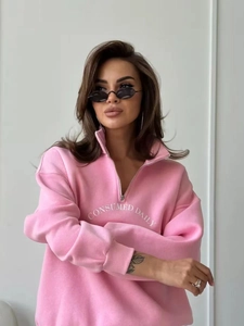 Detail eines rosa Sweatshirts mit halbem Reißverschluss und weißem Textdruck auf der Brust