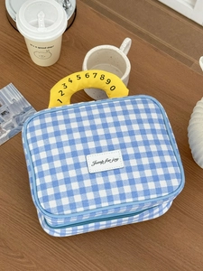 Blaue Kosmetiktasche mit Karomuster, gelbem Griff und Aufnäher auf einem Holztisch