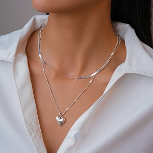 Close-up of double-layered silver heart pendant and snake chain necklace on a model