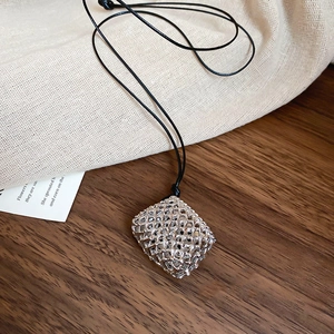 Macro detail of silver hollow cube pendant on black wax cord over rustic wood surface